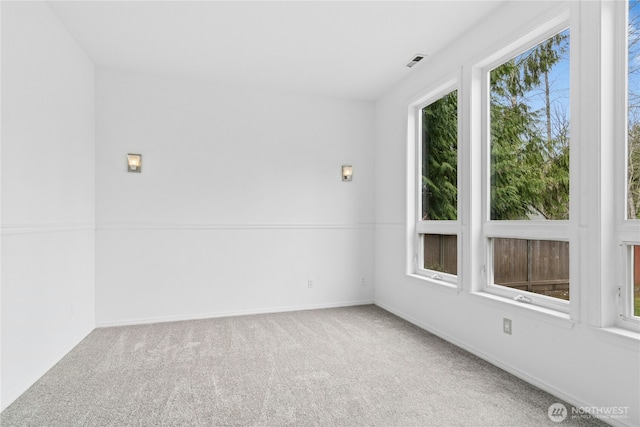 carpeted spare room featuring a wealth of natural light, visible vents, and baseboards