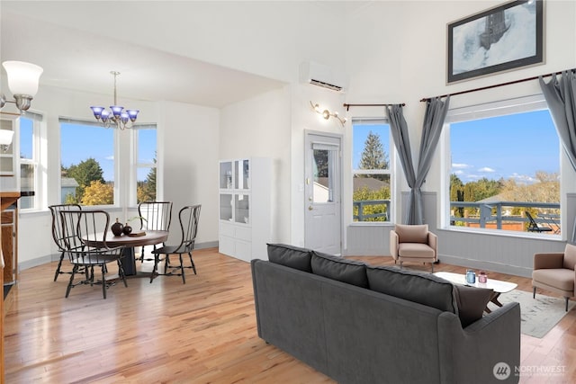 living area with baseboards, a wall unit AC, light wood finished floors, and an inviting chandelier