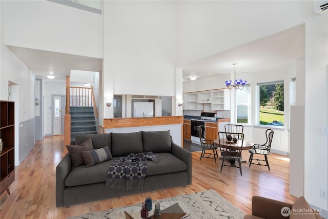 living area featuring light wood-style floors, stairs, a notable chandelier, and a wall mounted air conditioner