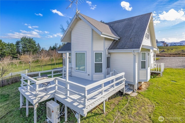 rear view of property featuring a deck, a lawn, and roof with shingles