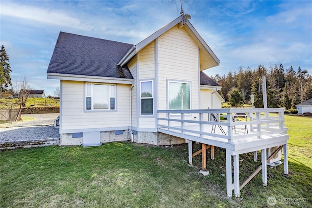 rear view of property with a shingled roof, a deck, and a lawn