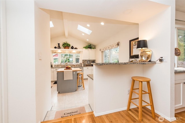 kitchen with lofted ceiling with skylight, light wood-style flooring, a breakfast bar area, and white cabinets