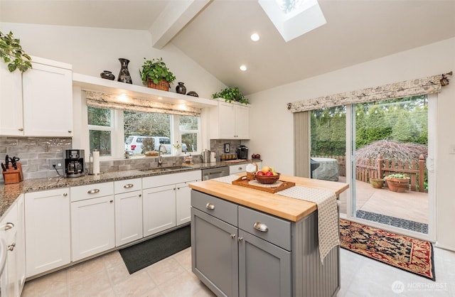 kitchen featuring lofted ceiling with skylight, butcher block countertops, backsplash, gray cabinets, and a sink