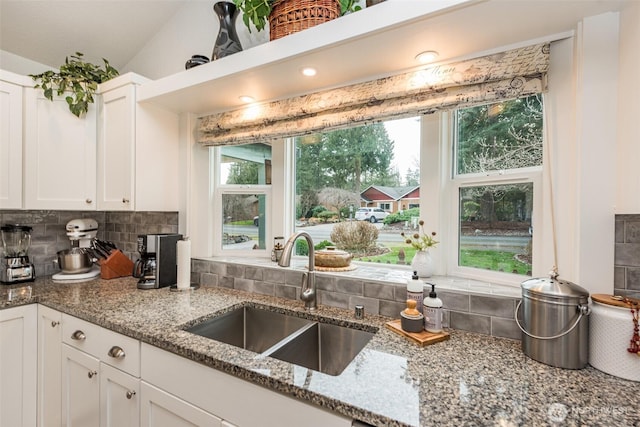 kitchen featuring stone countertops, a sink, white cabinetry, and decorative backsplash