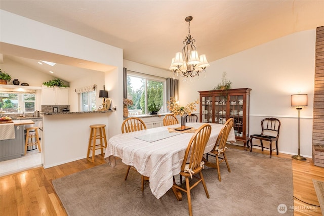 dining room with a healthy amount of sunlight, light wood-style floors, vaulted ceiling, and a notable chandelier