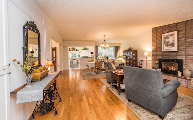 living area with light wood-type flooring, a brick fireplace, and a notable chandelier