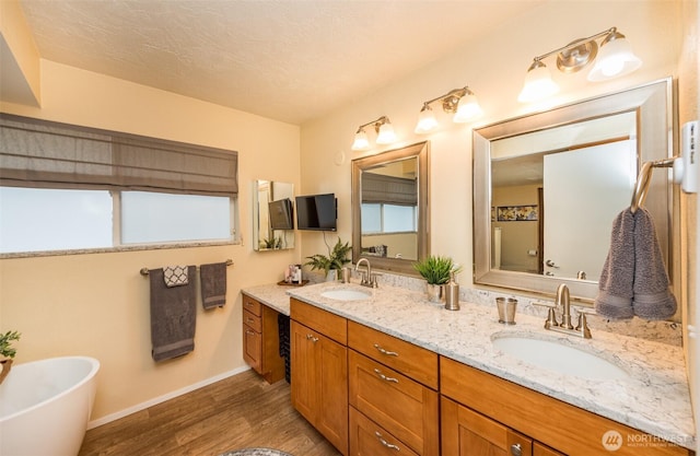 bathroom with double vanity, a soaking tub, a sink, and wood finished floors