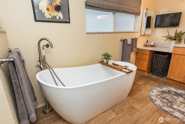 bathroom with a freestanding bath, wood finished floors, and vanity