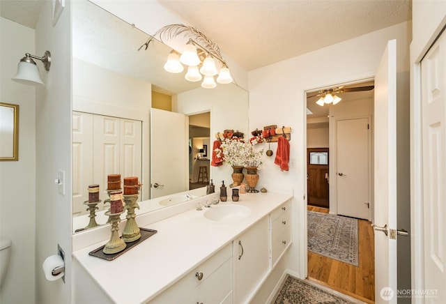 bathroom with ceiling fan, a textured ceiling, toilet, wood finished floors, and vanity