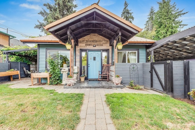 entrance to property featuring metal roof, a yard, fence, and a gate