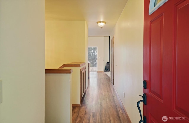 hallway featuring baseboards, wood finished floors, and an upstairs landing