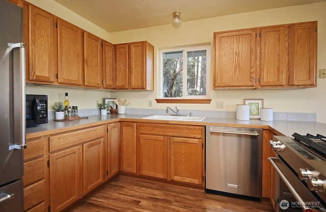 kitchen featuring stainless steel appliances, light countertops, brown cabinetry, dark wood-type flooring, and a sink