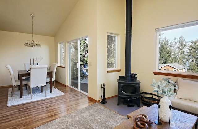 dining area with high vaulted ceiling, wood finished floors, baseboards, a wood stove, and an inviting chandelier