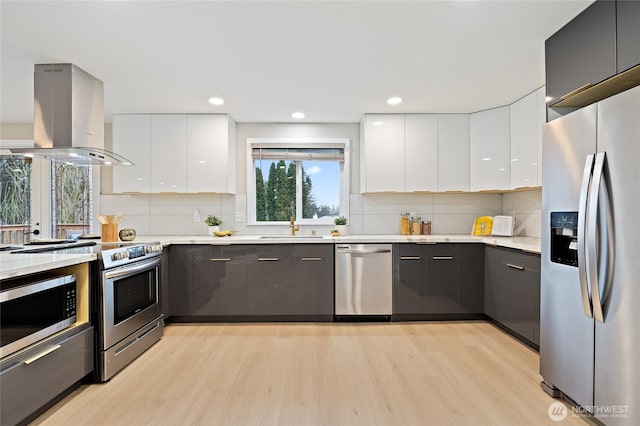 kitchen featuring light wood-type flooring, island exhaust hood, stainless steel appliances, white cabinetry, and modern cabinets