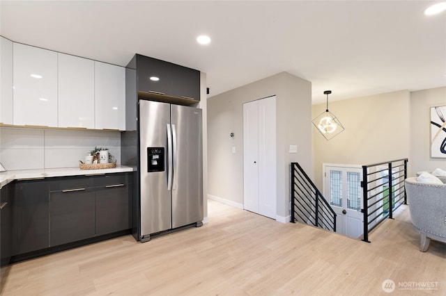 kitchen featuring decorative light fixtures, light countertops, light wood-type flooring, stainless steel fridge, and white cabinetry