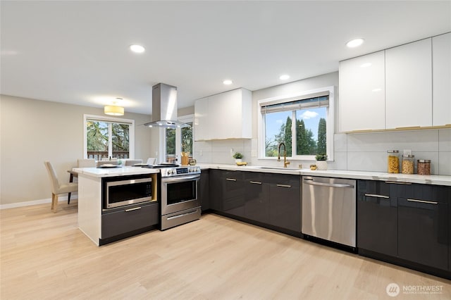 kitchen featuring appliances with stainless steel finishes, a peninsula, island range hood, modern cabinets, and a sink