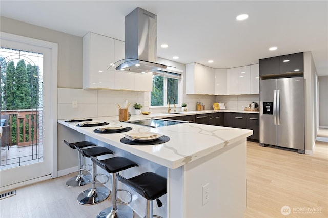 kitchen with a peninsula, island exhaust hood, stainless steel fridge, modern cabinets, and a sink