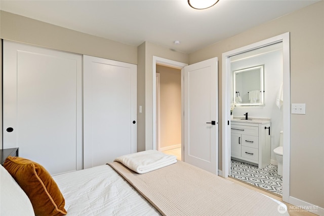 bedroom with a sink, a closet, baseboards, and ensuite bath