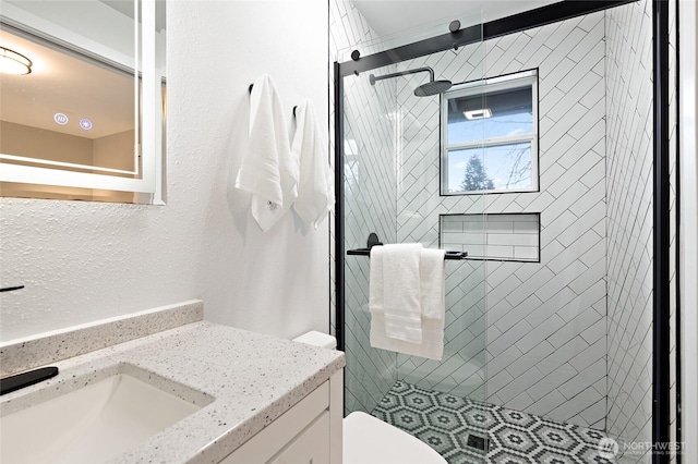 full bathroom with vanity, a shower stall, toilet, and a textured wall