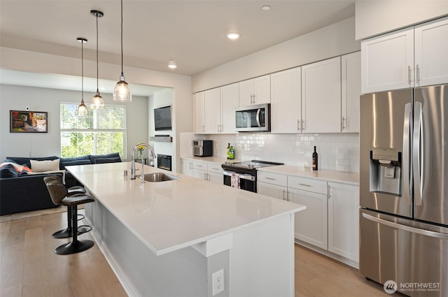 kitchen featuring light wood finished floors, backsplash, appliances with stainless steel finishes, white cabinets, and a sink