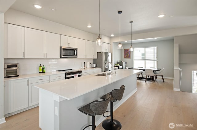 kitchen with decorative backsplash, an island with sink, light wood-style flooring, appliances with stainless steel finishes, and a sink