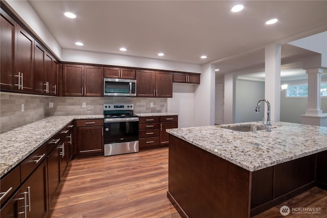 kitchen featuring light stone counters, appliances with stainless steel finishes, a sink, wood finished floors, and ornate columns