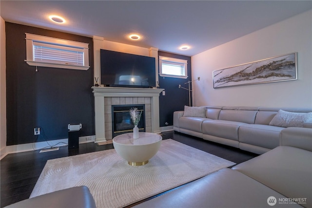 living area featuring a tiled fireplace, baseboards, and wood finished floors