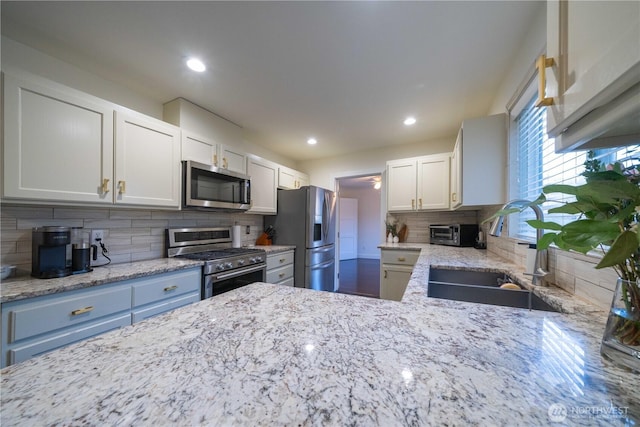 kitchen with light stone counters, tasteful backsplash, appliances with stainless steel finishes, white cabinetry, and a sink