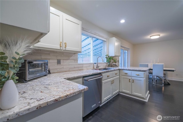 kitchen with dark wood-style floors, stainless steel dishwasher, white cabinetry, a sink, and a peninsula