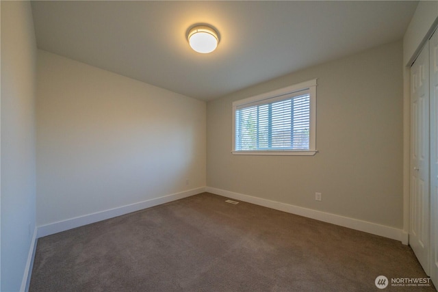 unfurnished bedroom with baseboards, dark colored carpet, and a closet