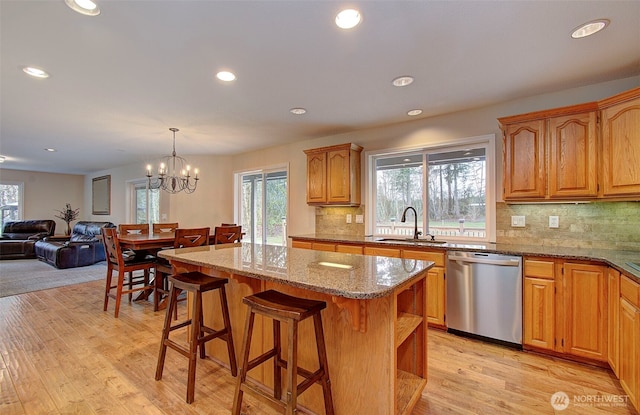 kitchen featuring a sink, a center island, light wood finished floors, light stone countertops, and dishwasher