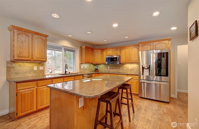 kitchen with light stone counters, light wood-style flooring, appliances with stainless steel finishes, and a sink