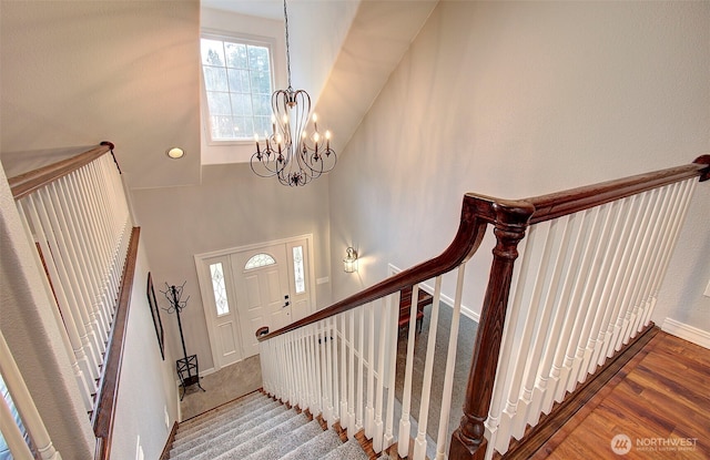 stairs featuring baseboards, wood finished floors, a high ceiling, and a chandelier