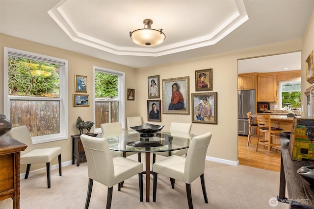 dining area featuring a wealth of natural light, light colored carpet, and a tray ceiling