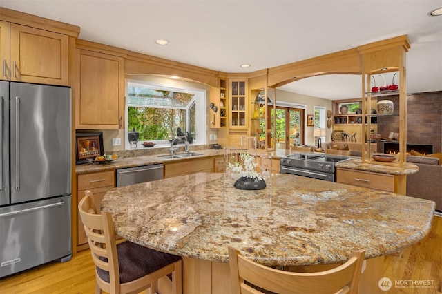 kitchen with a sink, light stone counters, open floor plan, a center island, and appliances with stainless steel finishes