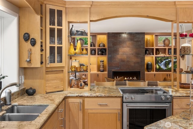 kitchen featuring light stone counters, a sink, stainless steel range, glass insert cabinets, and a tiled fireplace