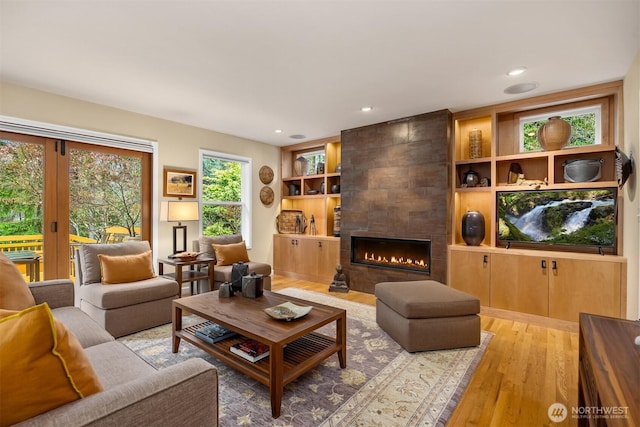 living room featuring built in features, recessed lighting, a tile fireplace, and light wood-type flooring