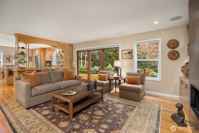 living room with recessed lighting, baseboards, light wood-type flooring, and a large fireplace