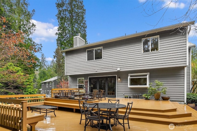 rear view of property featuring a deck, a chimney, and outdoor dining space