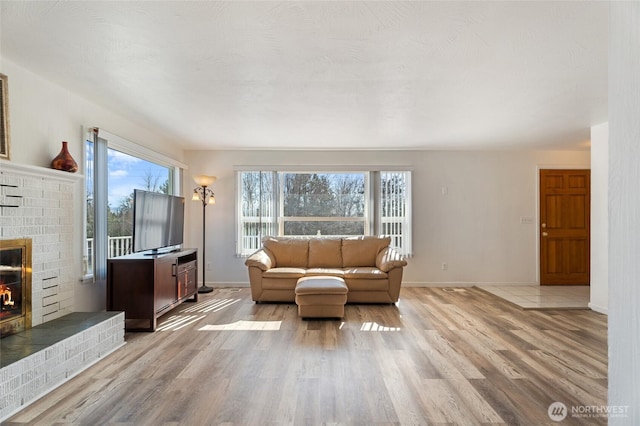 living room with light wood-type flooring, baseboards, and a brick fireplace