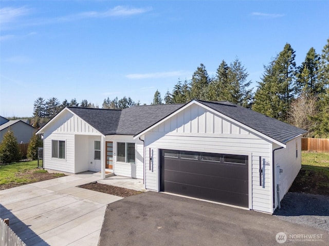 view of front of house with driveway, a garage, a shingled roof, fence, and board and batten siding