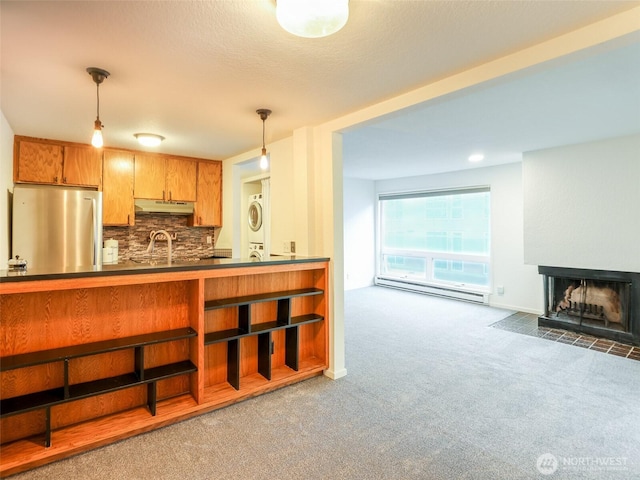 kitchen with stacked washer / drying machine, freestanding refrigerator, baseboard heating, under cabinet range hood, and a sink