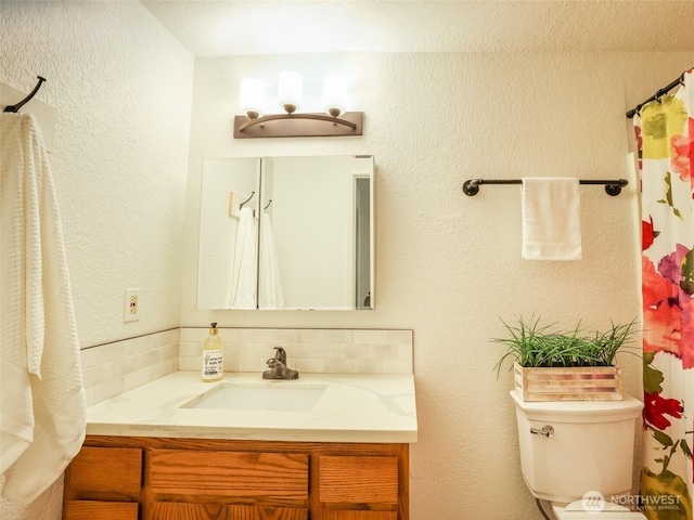 full bath featuring toilet, a textured wall, and vanity