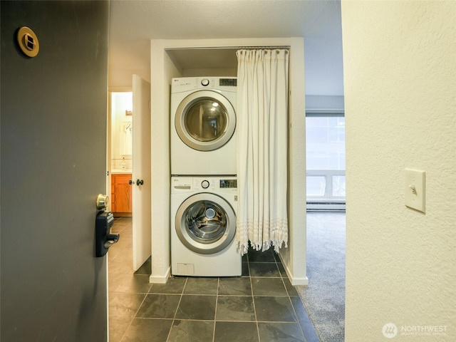 laundry area featuring dark carpet, stacked washing maching and dryer, laundry area, dark tile patterned floors, and baseboards