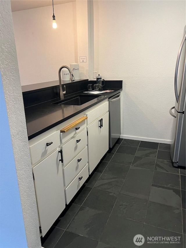 kitchen featuring stainless steel appliances, dark countertops, white cabinets, a sink, and baseboards