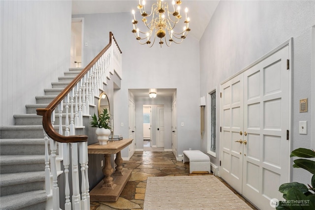 entrance foyer with baseboards, a towering ceiling, stone tile floors, and stairs