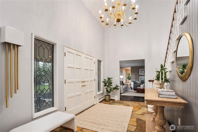 entryway featuring a baseboard radiator, an inviting chandelier, stone tile floors, and a high ceiling