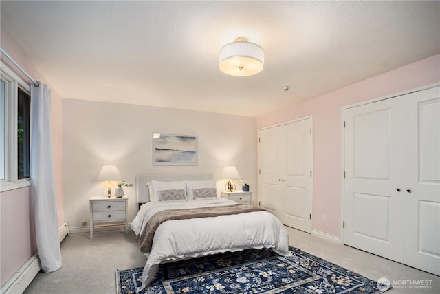 bedroom featuring a baseboard heating unit, multiple closets, baseboards, and light colored carpet