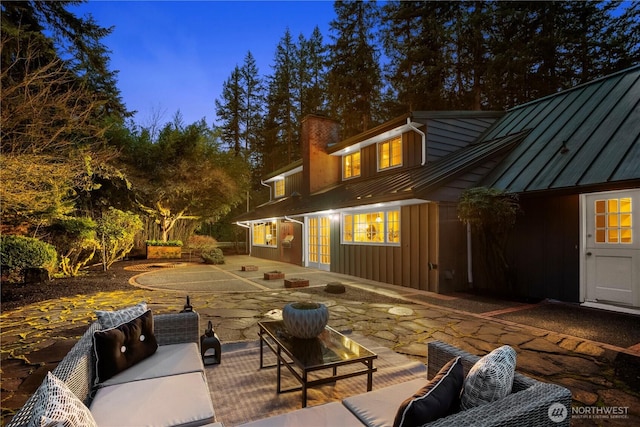 back of property featuring a chimney, outdoor lounge area, a standing seam roof, a patio area, and metal roof