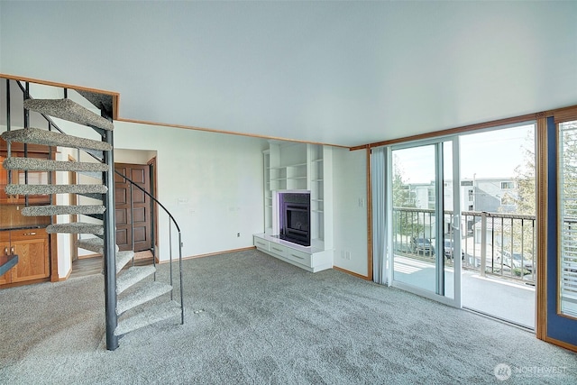 unfurnished living room with carpet floors, a glass covered fireplace, expansive windows, baseboards, and stairs